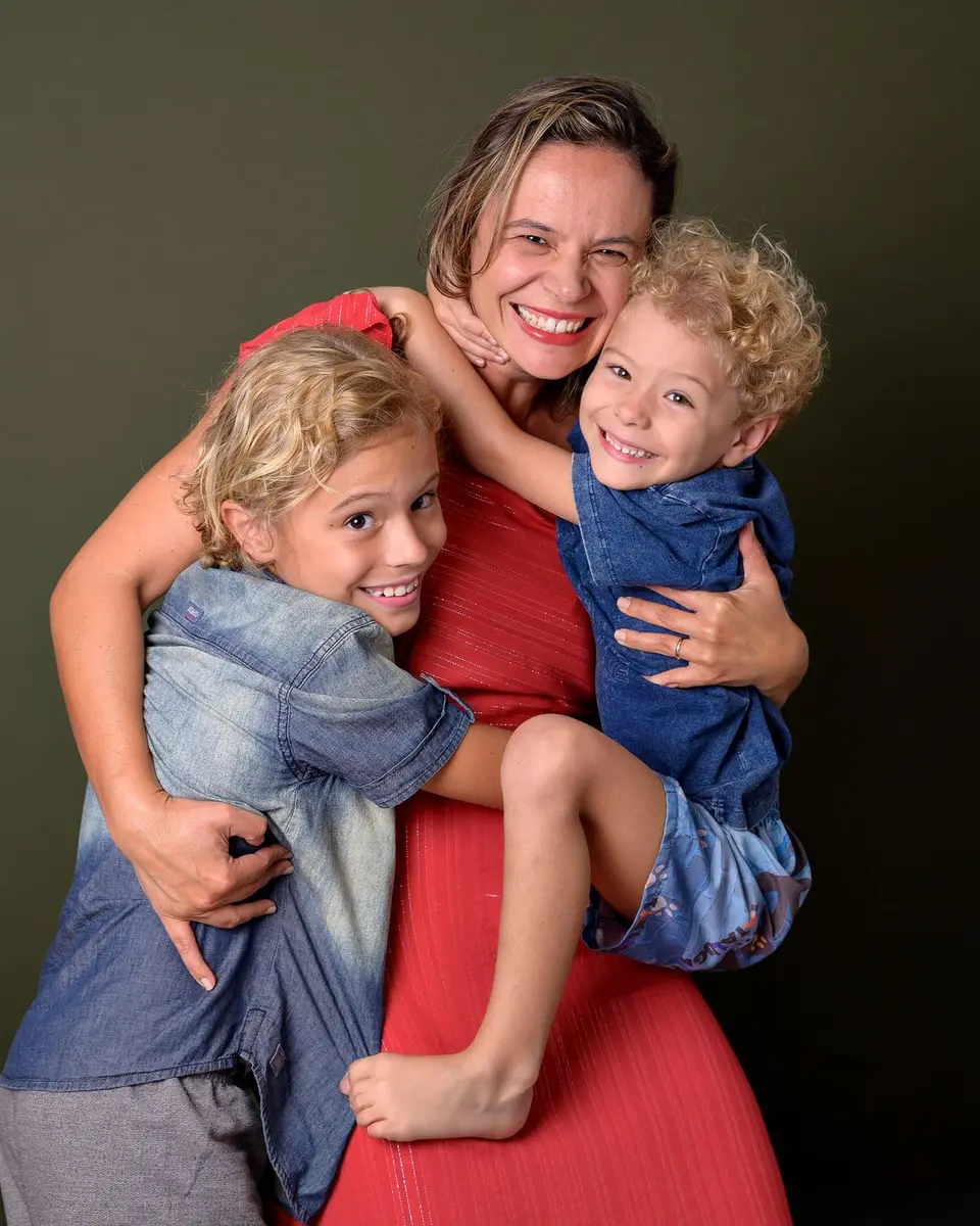 A joyful mother embraces her smiling children against a green backdrop.