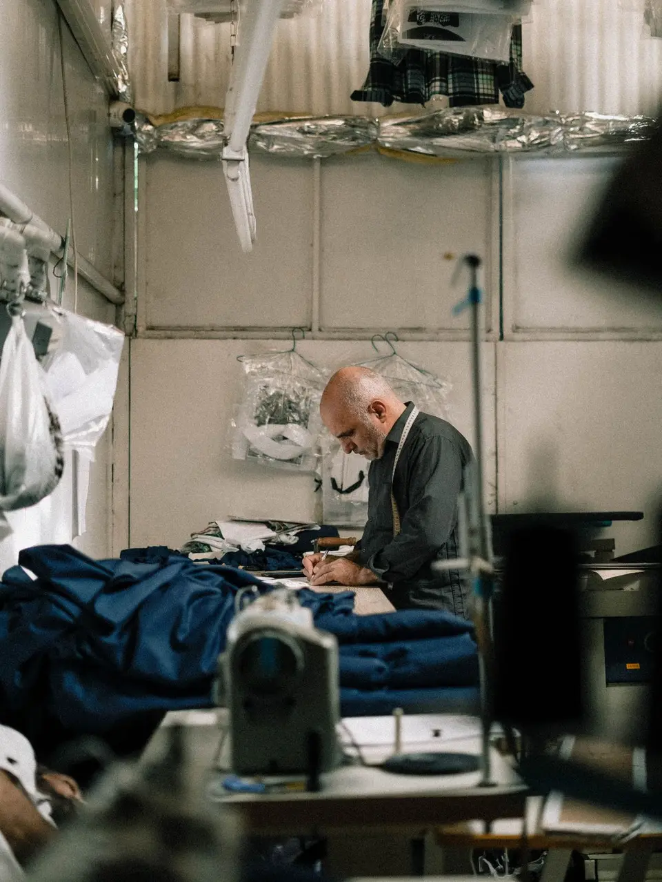A skilled tailor focuses on sewing in his workshop filled with fabrics and sewing equipment.