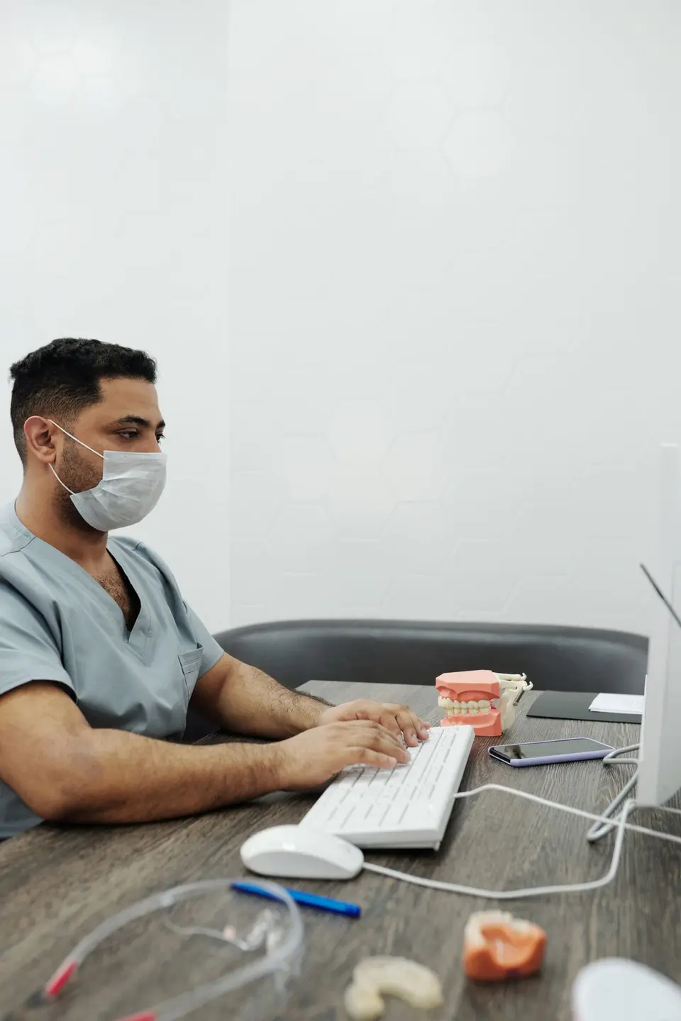 A dentist wearing a face mask types on a computer in a clinic setting.