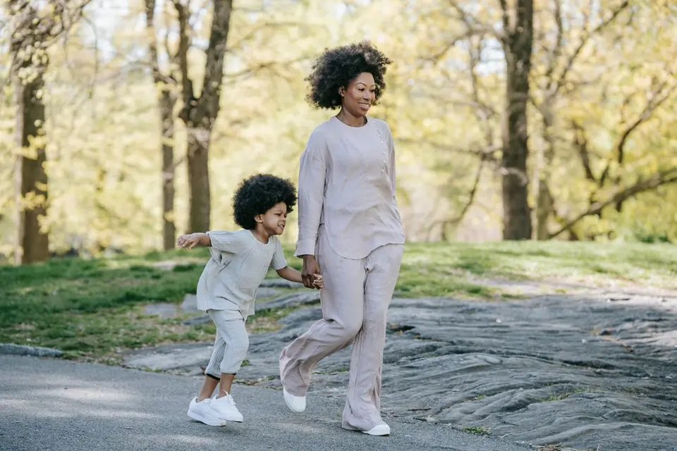 A joyful mother and son holding hands while walking in a sunny spring park.