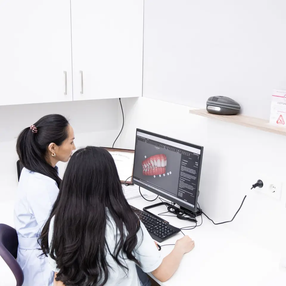 Two female dentists in a clinic reviewing 3D dental images on a computer for precise diagnostic evaluations.